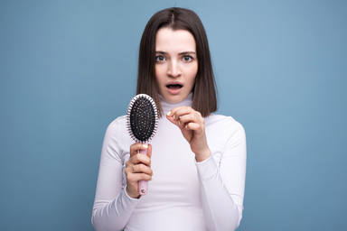 A brunette with a comb in her hands is worried about hair loss. Studio portrait blue background.
